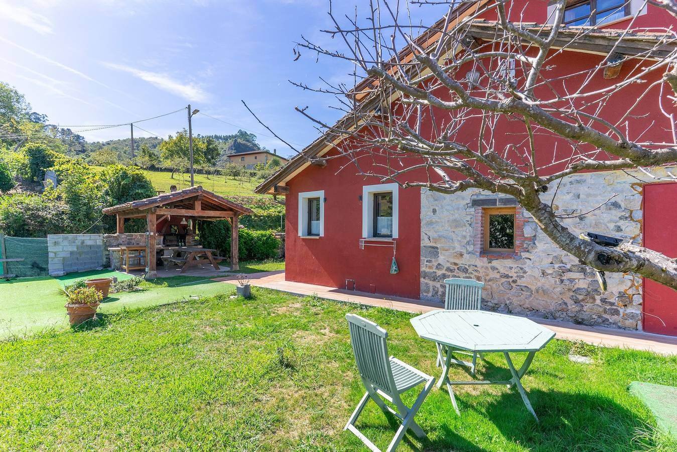 Jardín con mesa y sillas blancas junto a la casa roja