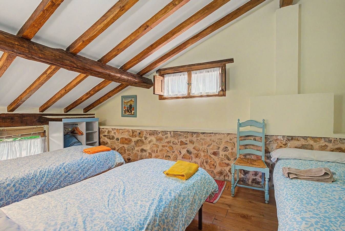 Dormitorio de la buhardilla con varias camas y pared de piedra